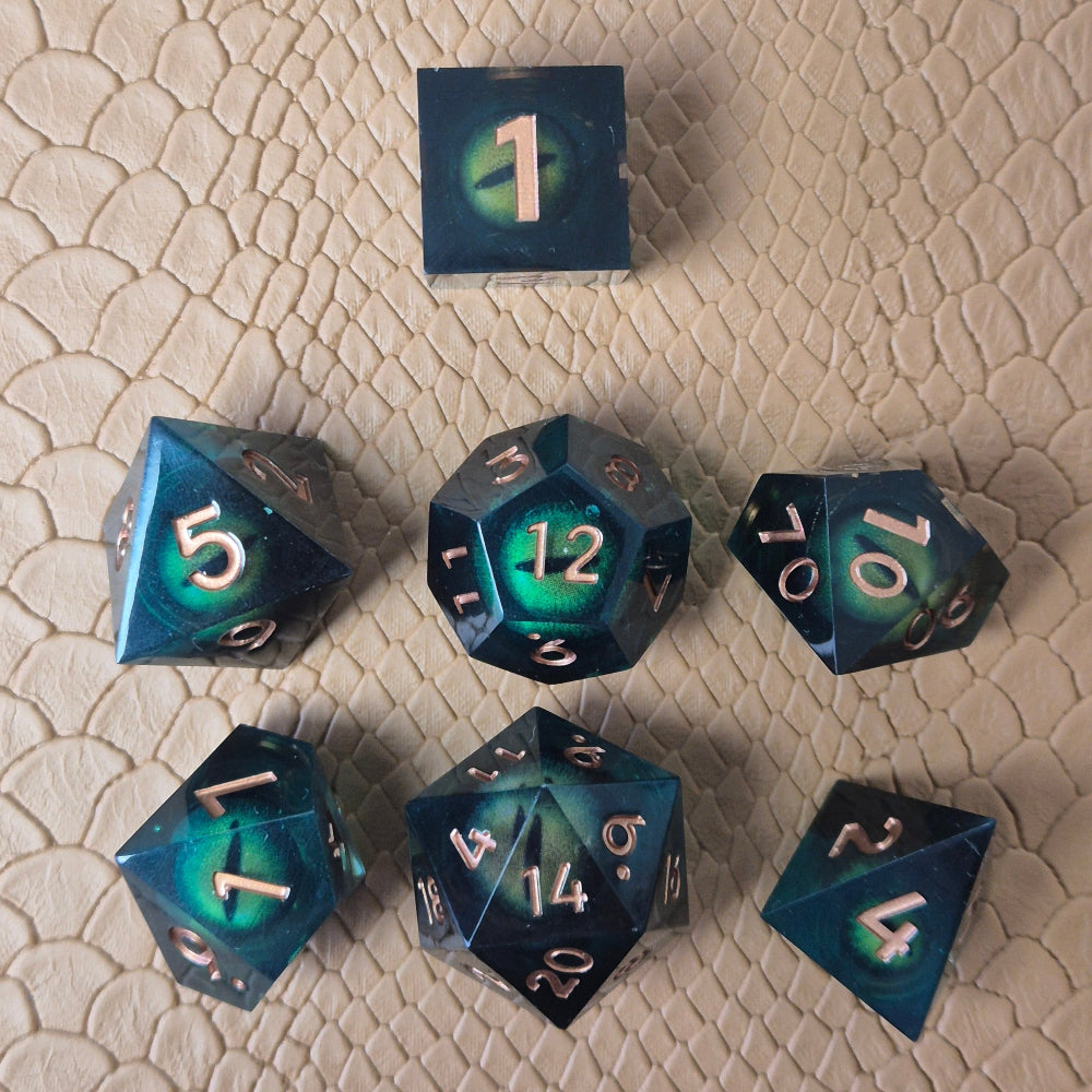 A set of clear green tinted liquid core resin dice with moving dragon eye inside and gold numbers engraved, displayed on a beige scale surface