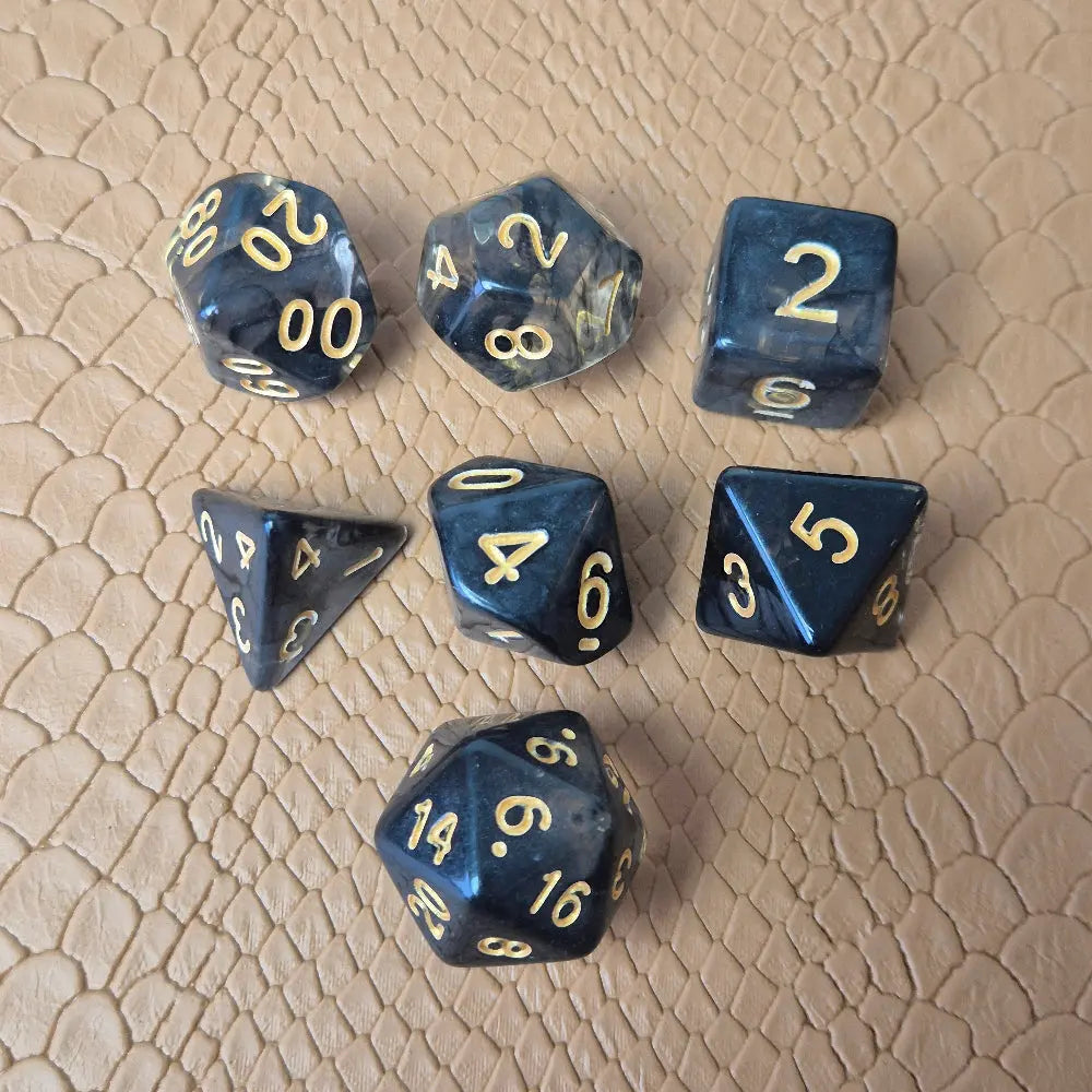 A set of clear black tinted polymere acrylic dice with gold numbers on a textured beige surface