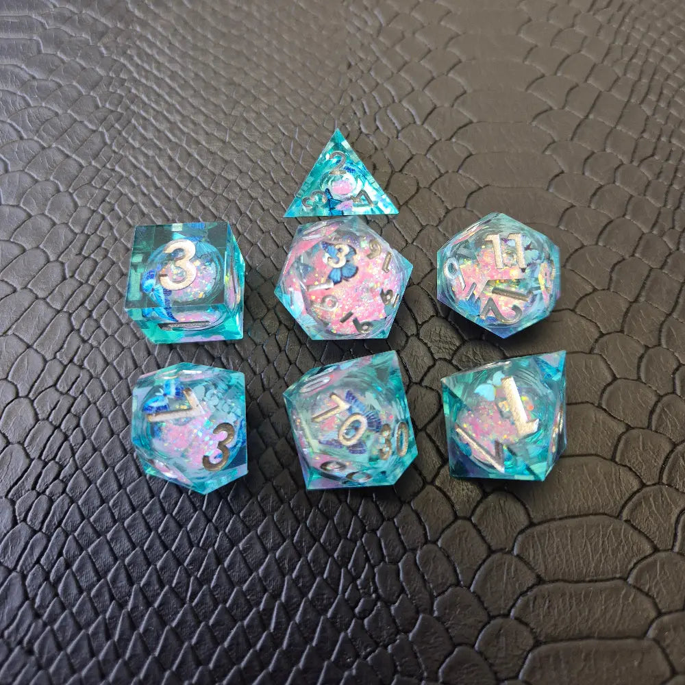 A set of light blue resin dice with pink liquid core and blue butterflies, displayed on black textured background