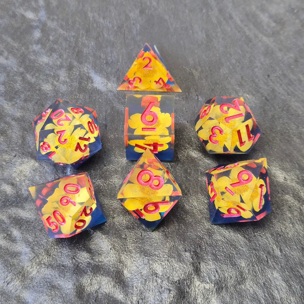 A set of clear sharp-edge resin dice with blue ground color and yellow flower inside on a black surface