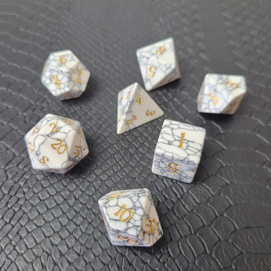 Set of white marble-textured gemstone dice with gold numbering, displayed on a black leather surface.