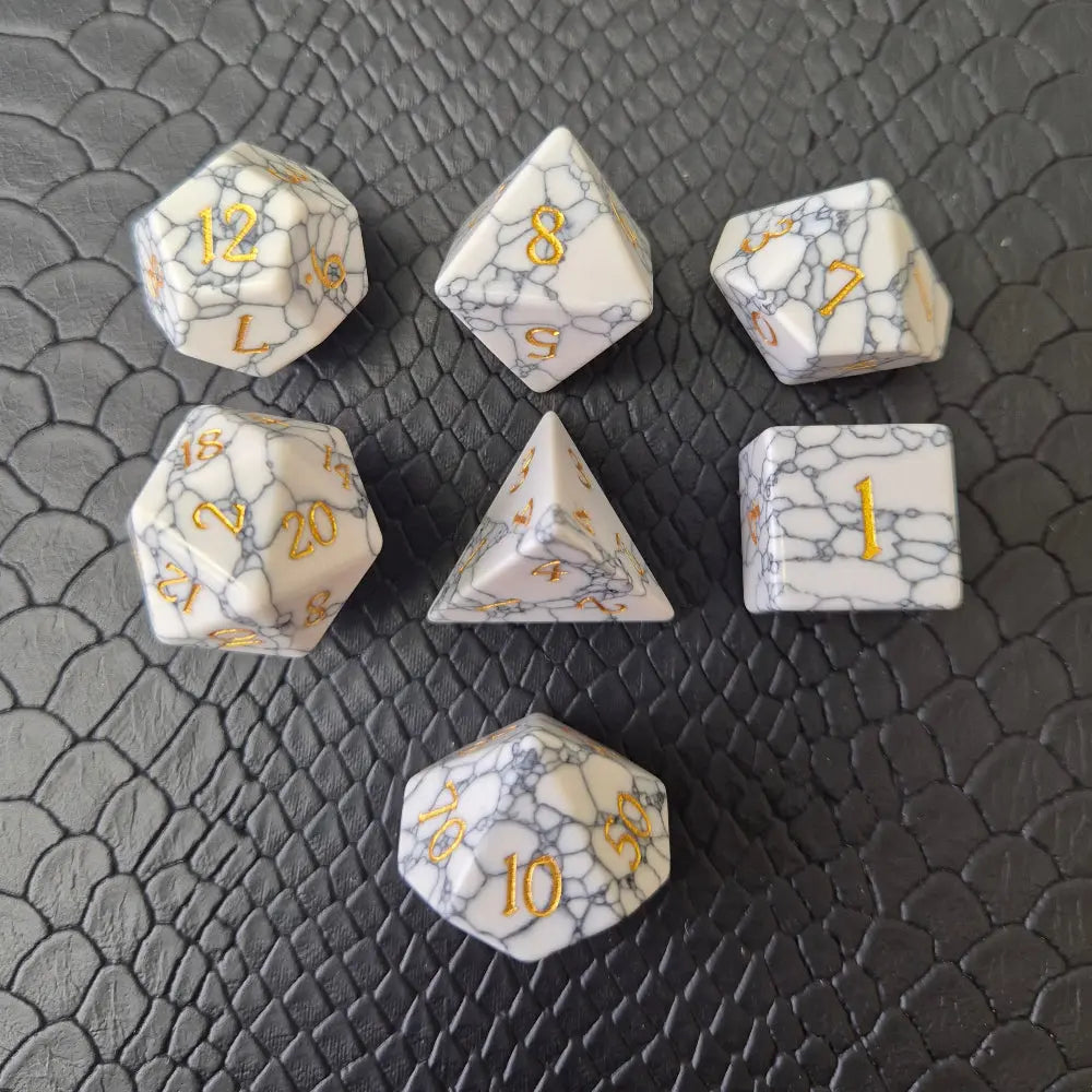 Set of white marble-textured gemstone dice with gold numbering, displayed on a black leather surface.