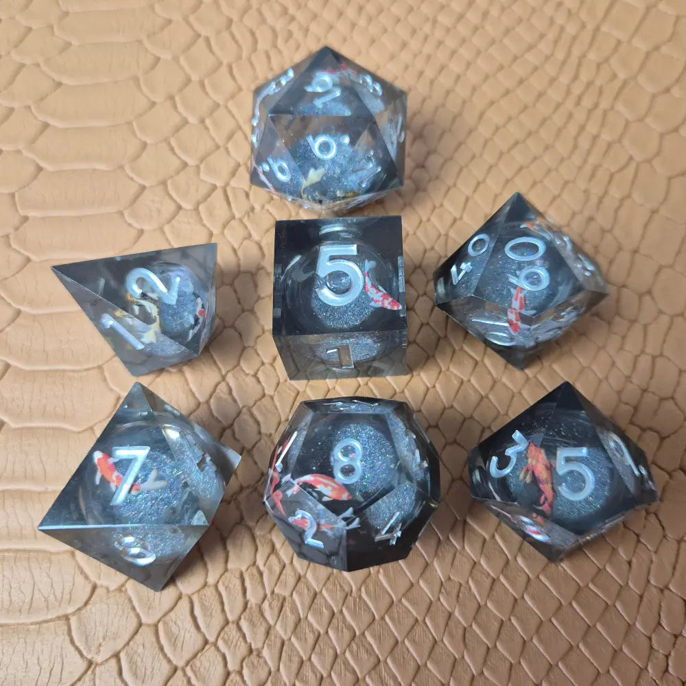 A set of clear grey tinted liquid core resin dice with koi fish inside filled with glitters on a beige textured surface