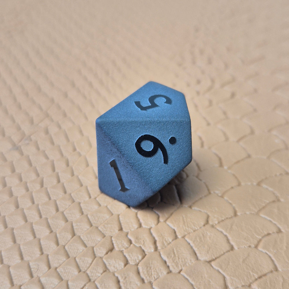 A set of matte black/ dark grey gemstone dice on a beige textured surface