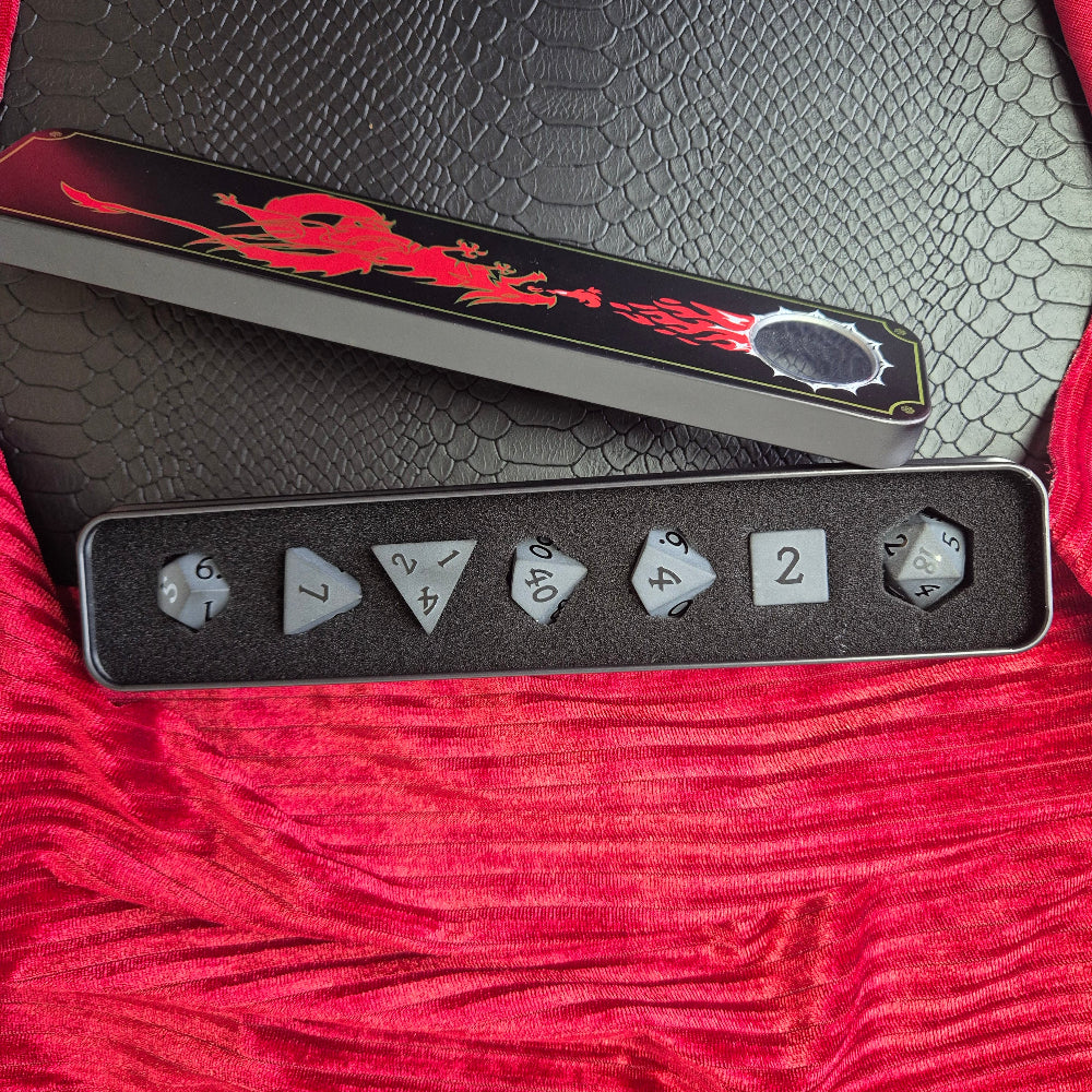A set of matte black/ dark grey gemstone dice on a beige textured surface