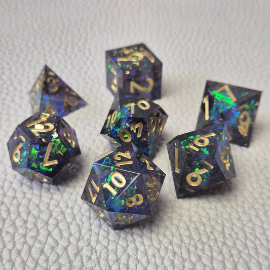 A set of blue sharp edge resin dice with green confetti inside on a white textured surface