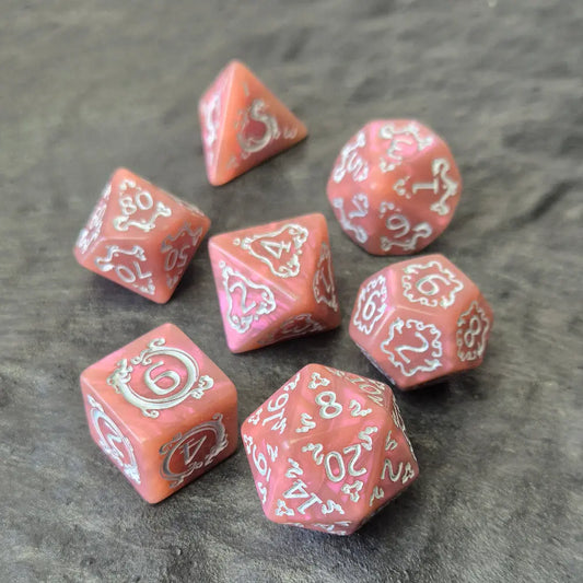 Pink acrylic D&D dice set with white arcane-style numbers and elegant swirls, displayed on a textured grey surface.