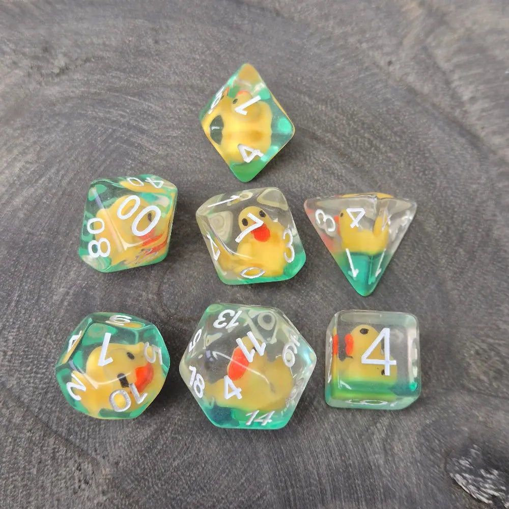Close-up of transparent resin dice with tiny yellow ducks inside, placed on a textured stone surface.