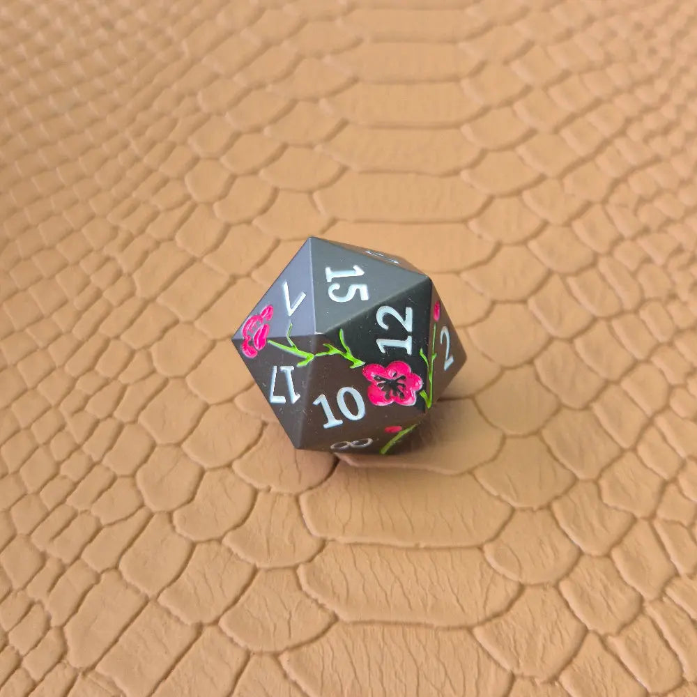 A black metal d20 dice on a brown dragon-like surface.