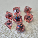 A set of red tinted clear liquid core dice with a moving dragon eye inside on a white textured background