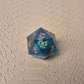 A set of clear green tinted liquid core resin dice with moving dragon eye inside and gold numbers engraved, displayed on a beige scale surface