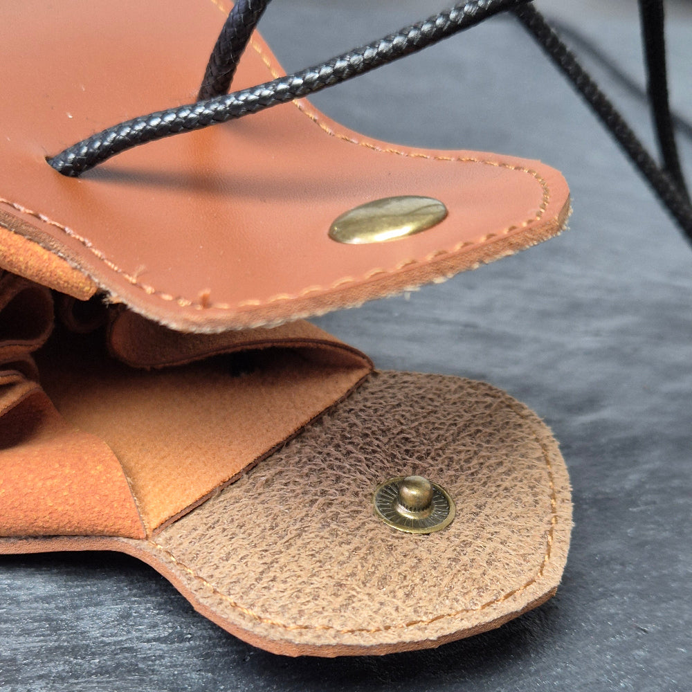 A brown leather dice bag with buttons and rope to tightly close it. Displayed on a black textured background