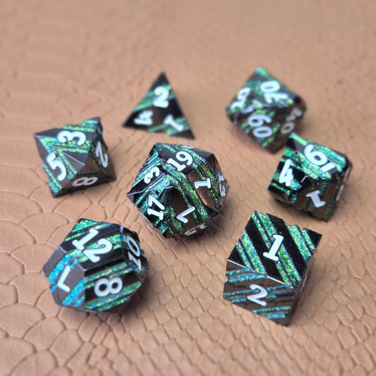 A set of black metal dice with shimmering green stripes and white numbering, displayed on a textured surface.