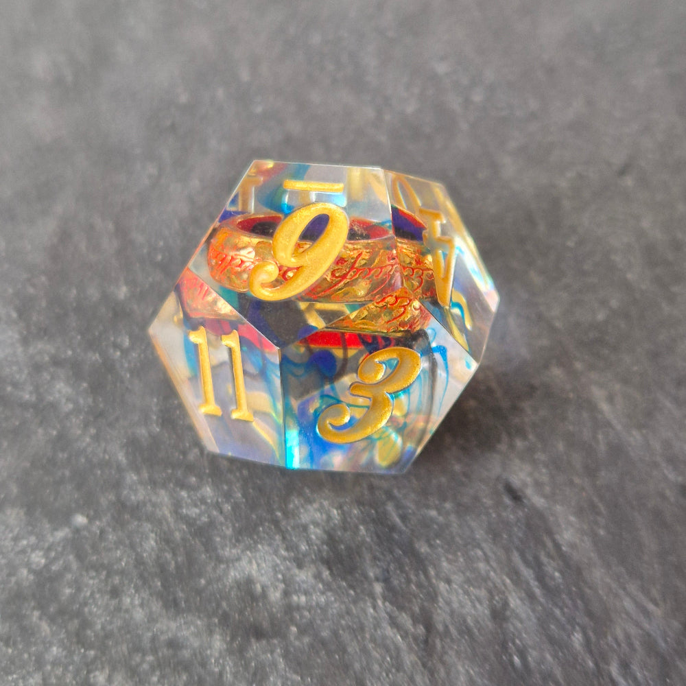 A set of clear blue tinted sharp edge resin dice with an engraved golden ring inside on a black surface