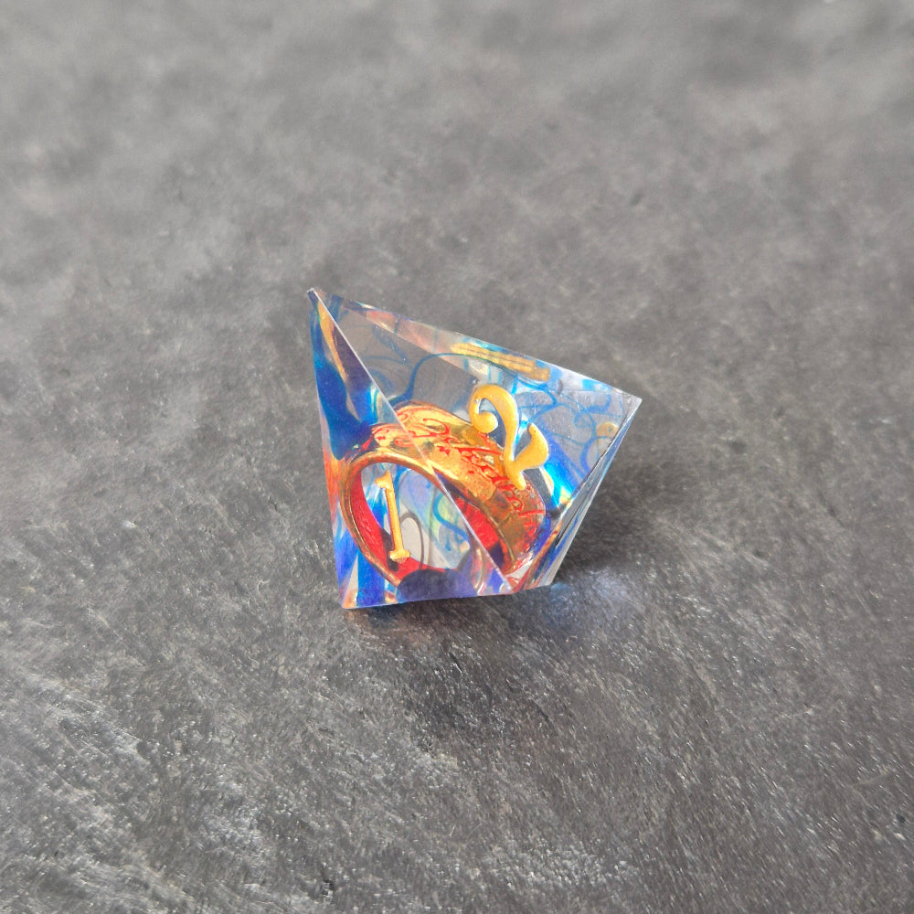 A set of clear blue tinted sharp edge resin dice with an engraved golden ring inside on a black surface