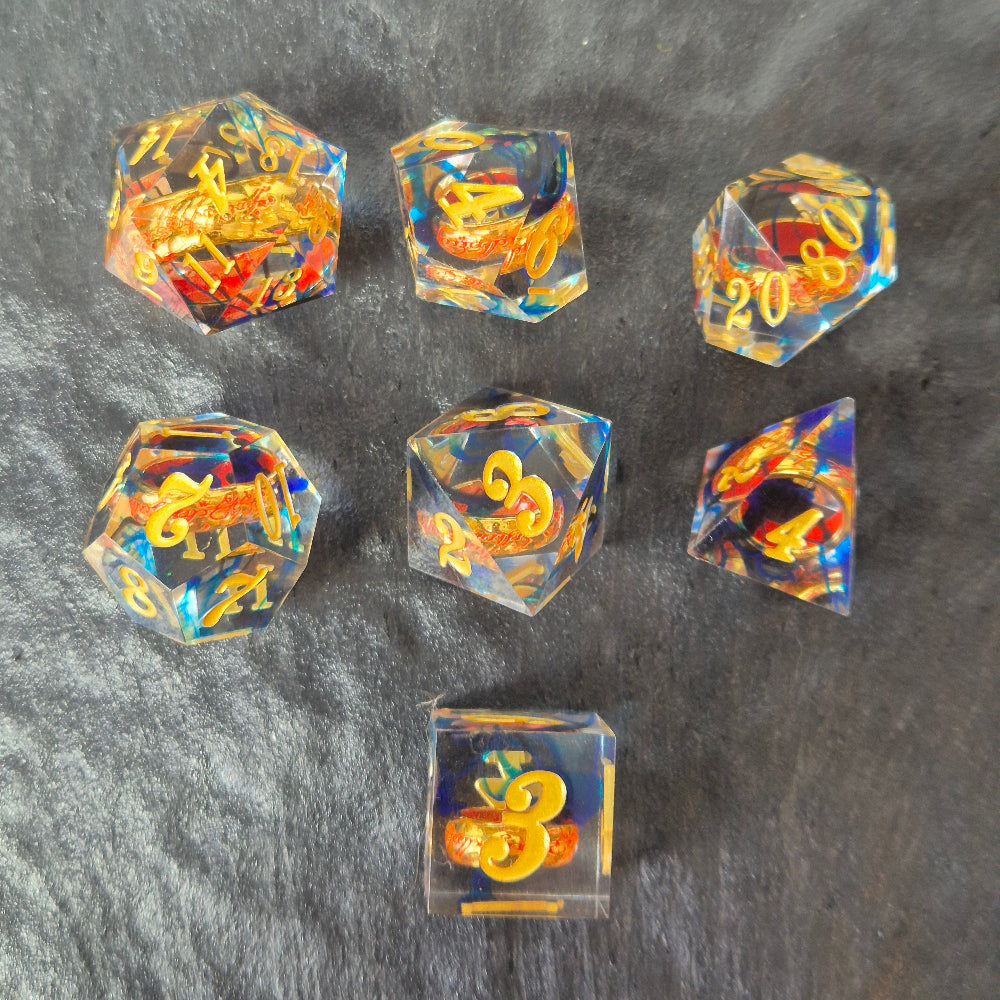 A set of clear blue tinted sharp edge resin dice with an engraved golden ring inside on a black surface