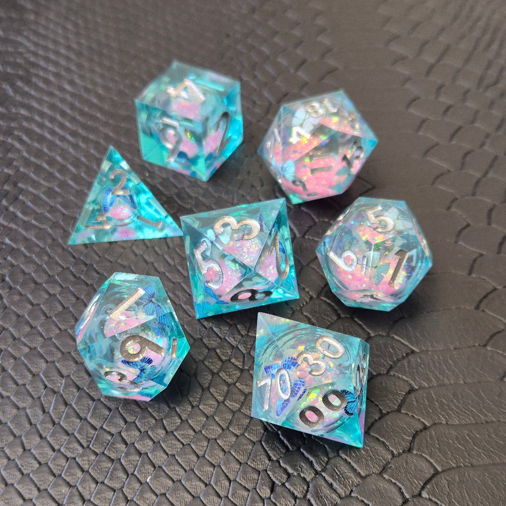 A set of light blue resin dice with pink liquid core and blue butterflies, displayed on black textured background