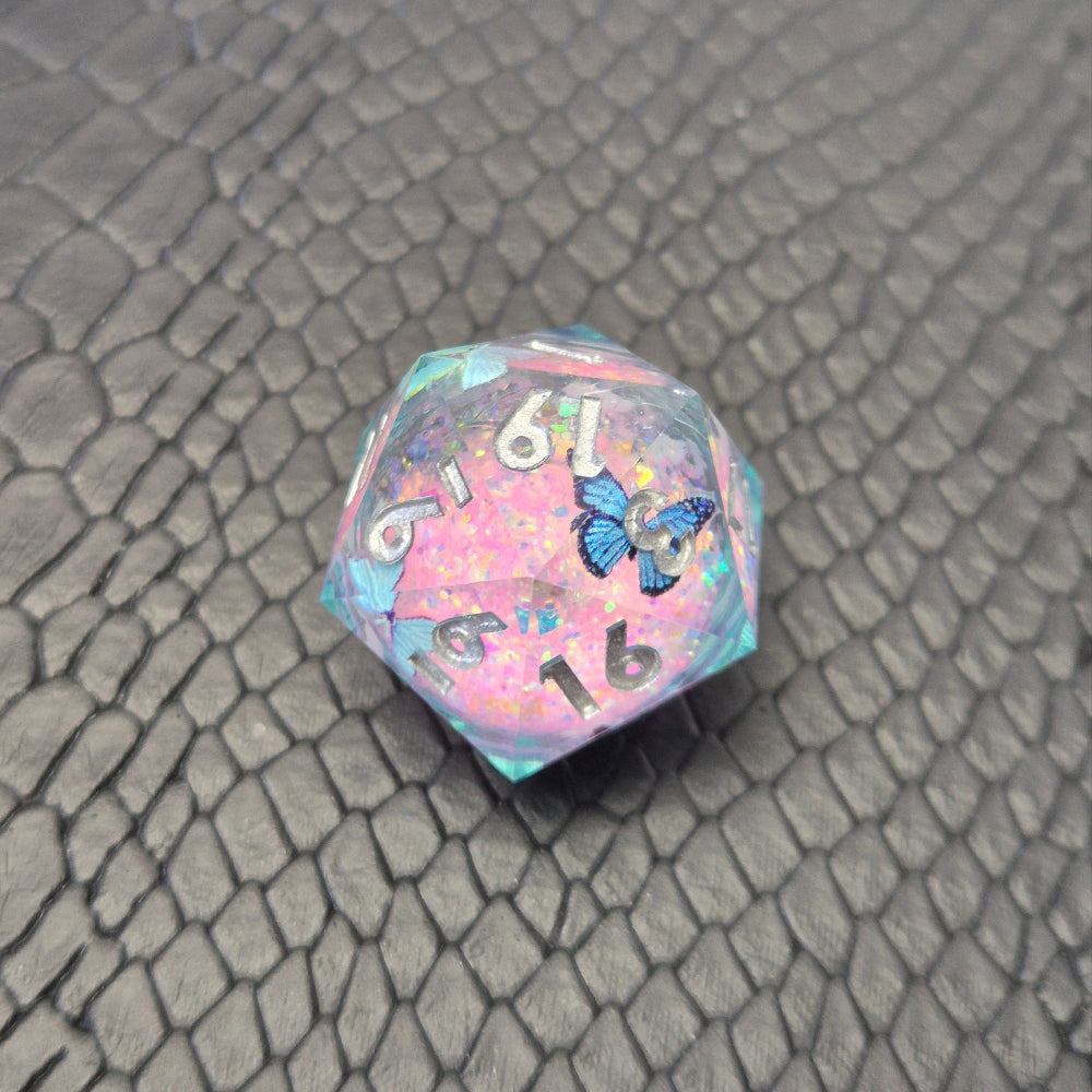 A set of light blue resin dice with pink liquid core and blue butterflies, displayed on black textured background