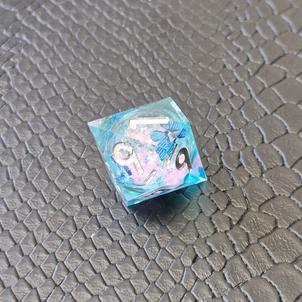 A set of light blue resin dice with pink liquid core and blue butterflies, displayed on black textured background