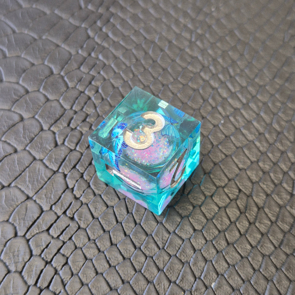 A set of light blue resin dice with pink liquid core and blue butterflies, displayed on black textured background