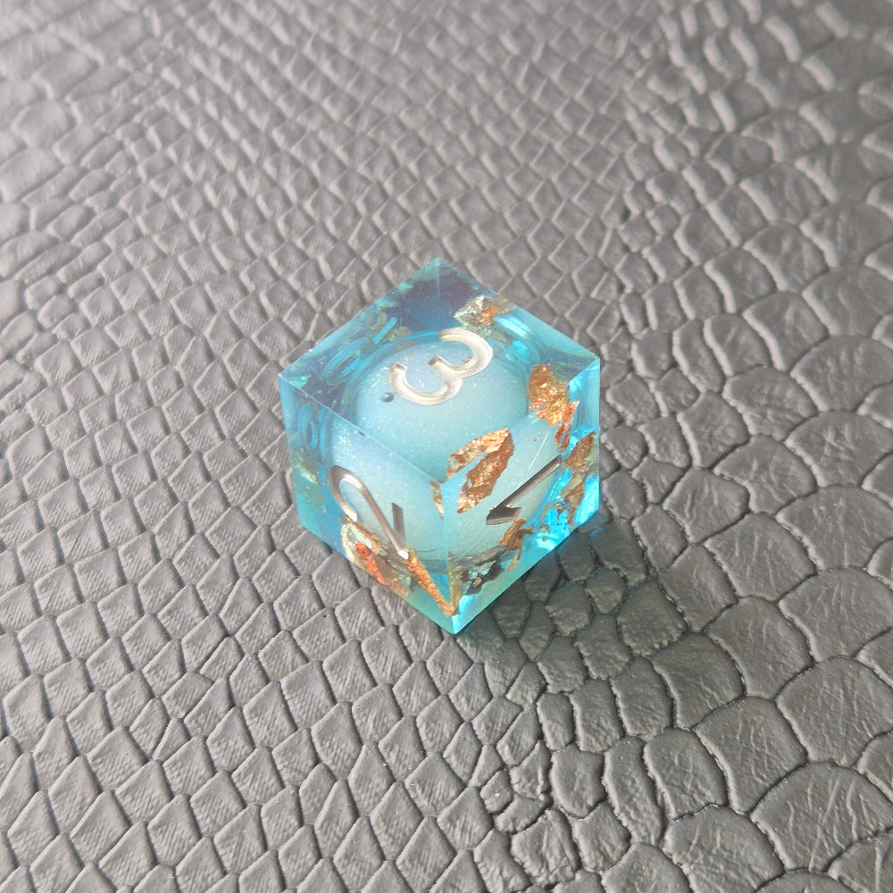 A set of clear light blue tinted liquid core dice with floating bronze flakes and white numbers, displayed on a black textured surface