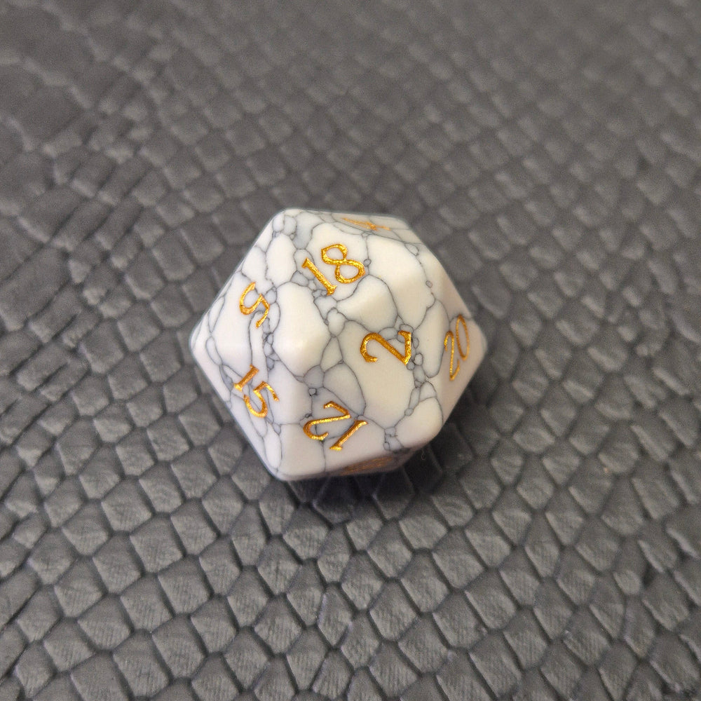 D20 white marble-textured gemstone die with gold numbering, displayed on a black leather surface.