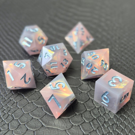 A set of pink sharp edge resin dice with blue numbers on a black textured surface