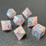 A set of pink sharp edge resin dice with blue numbers on a black textured surface