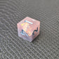 A set of pink sharp edge resin dice with blue numbers on a black textured surface