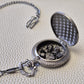 A silver coloured full metal pocket watch themed dice locket, with engraved backside and detailed kraken on the front. Contains full set of metal dice inside