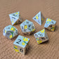 Metal D&D dice set with matte silver finish and painted yellow flowers, displayed on textured leather background.