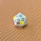 Metal D&D dice set with matte silver finish and painted yellow flowers, displayed on textured leather background.