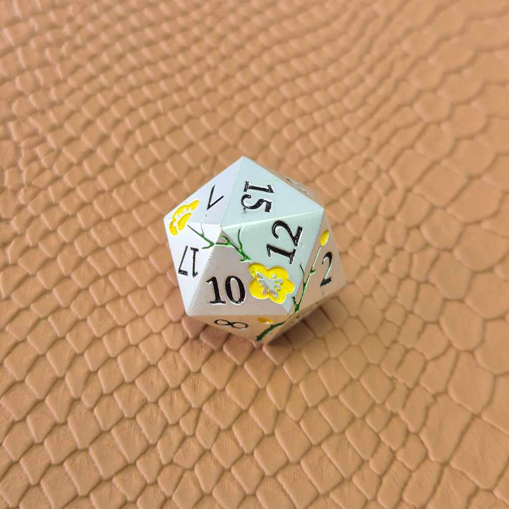 Metal D&D dice set with matte silver finish and painted yellow flowers, displayed on textured leather background.