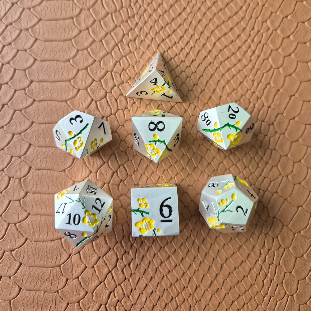 Metal D&D dice set with matte silver finish and painted yellow flowers, displayed on textured leather background.