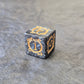 Acrylic D6 dice with swirling black design and ornate golden numbering, displayed on a dark background.