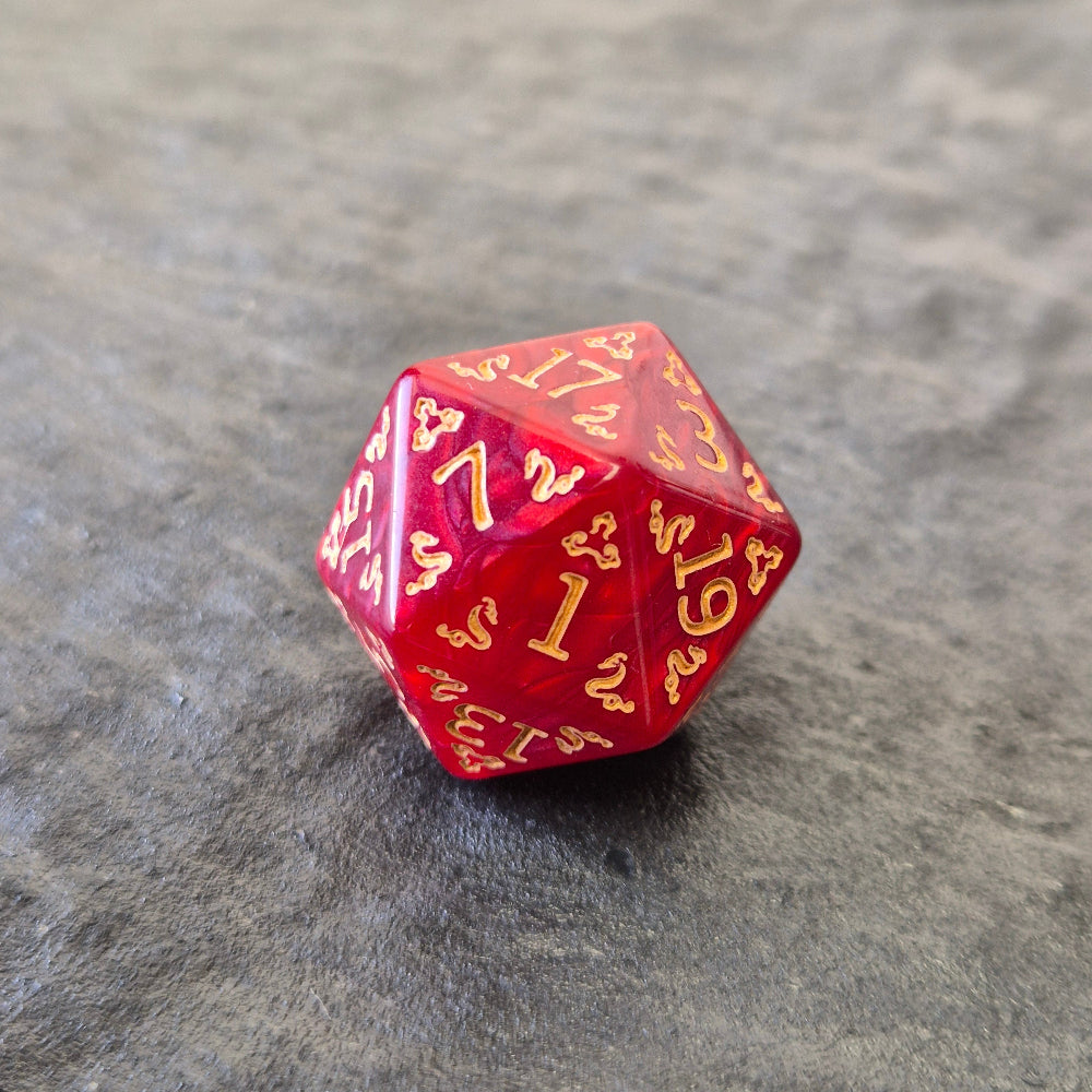 Red acrylic D20 with golden arcane-style numbers and swirling patterns, displayed on a textured grey background.