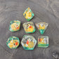 Close-up of transparent resin dice with tiny yellow ducks inside, placed on a textured stone surface.