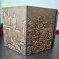 Foldable four-panel Dungeon Master screen with embossed fantasy scenes and included felt sleeve, displayed on a dark tabletop.